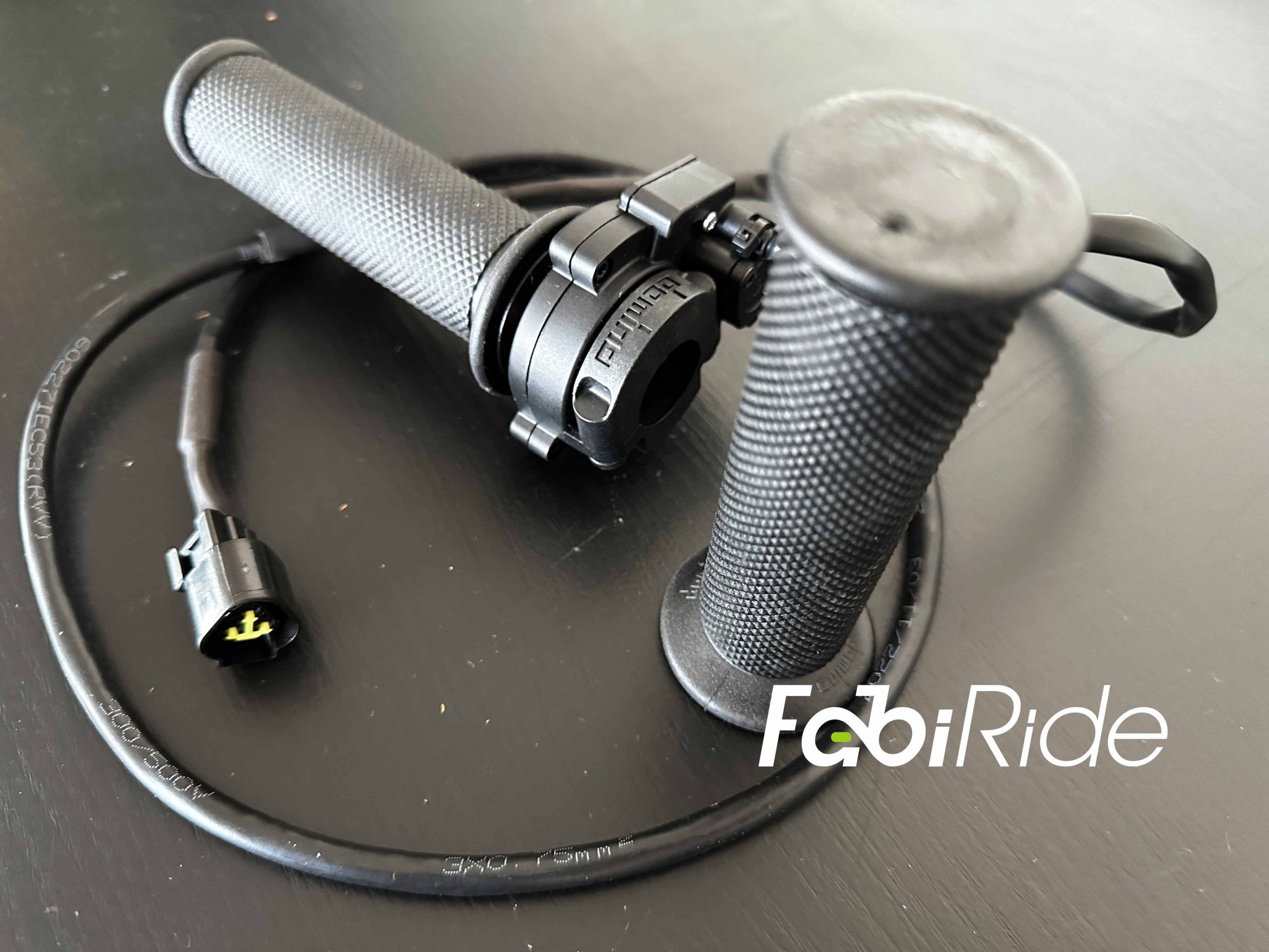Juodos guminės elektrinio motociklo vairo rankenos (grips) su prijungimo laidu „FabiRide“ fone.